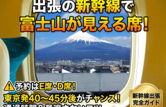 新幹線の窓から見える、青空と裾野まで広がる美しい富士山の景色。手前のE席の座席テーブルにはノートパソコンやコーヒーが置かれており、30代のスーツを着たビジネスパーソンが移動中に窓の外を眺めながら、リフレッシュや撮影を行っている様子。