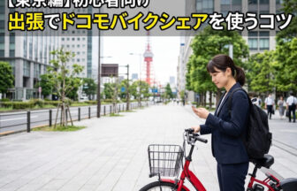東京のオフィス街にあるドコモ・バイクシェアのポートで、赤い電動アシスト自転車の解錠やバッテリーのチェックをスマートフォンで行う、スーツ姿にビジネスリュックのビジネスパーソン。